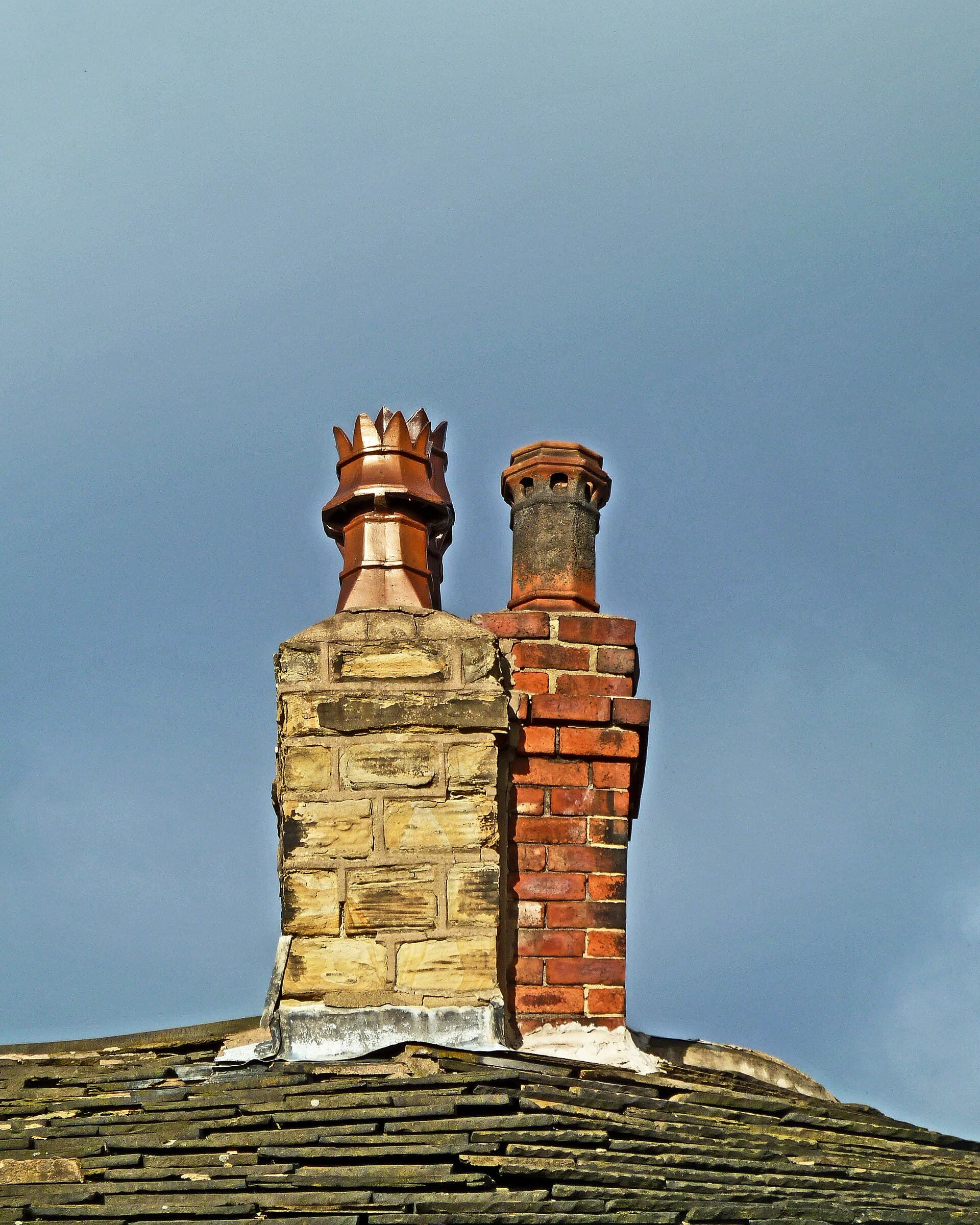 Two chimney stacks, one stone and one brick, each with a clay pot on top