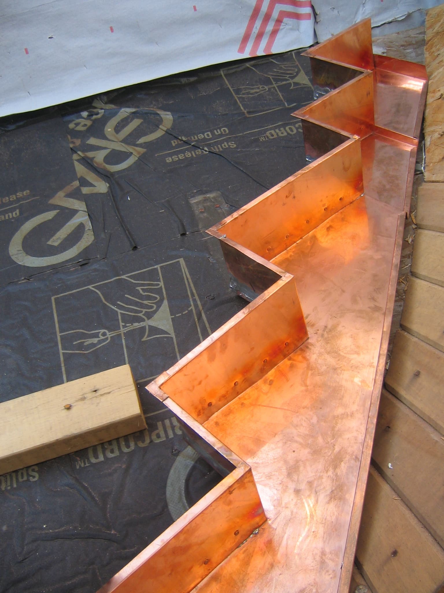 Zig-zag step flashing made of copper sheet laid against a wall on a roof deck