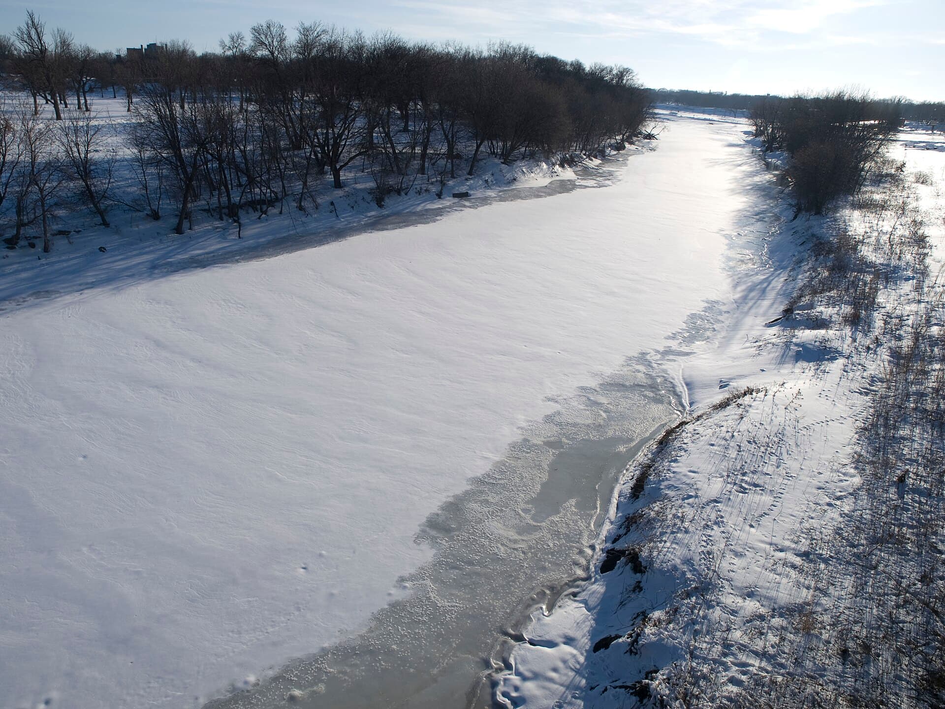 The frozen Red River of the North under snow, with bare trees along its banks